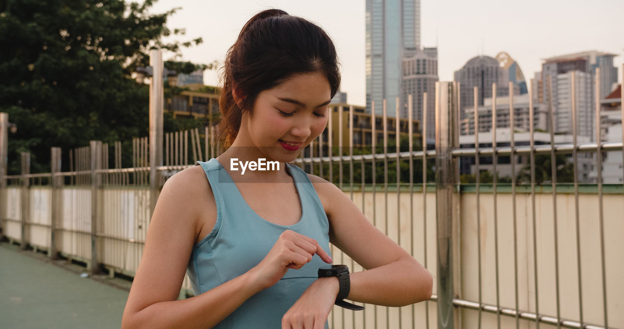 Beautiful young woman using smart watch in city