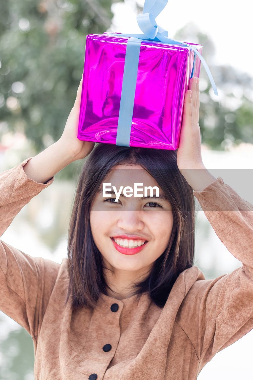 Cheerful attractive young woman put the purple christmas gift box on head with full of happiness