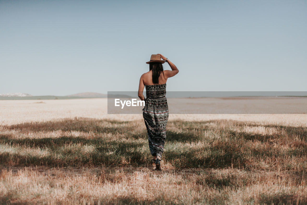 Rear view of woman walking on field against clear sky