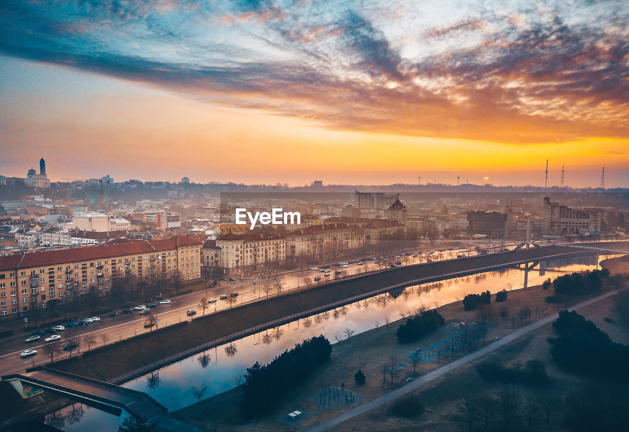 Buildings by river against sky at sunset