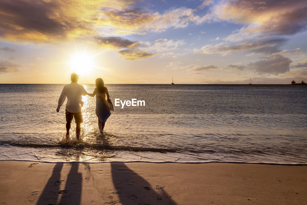 rear view of woman walking on beach against sky during sunset