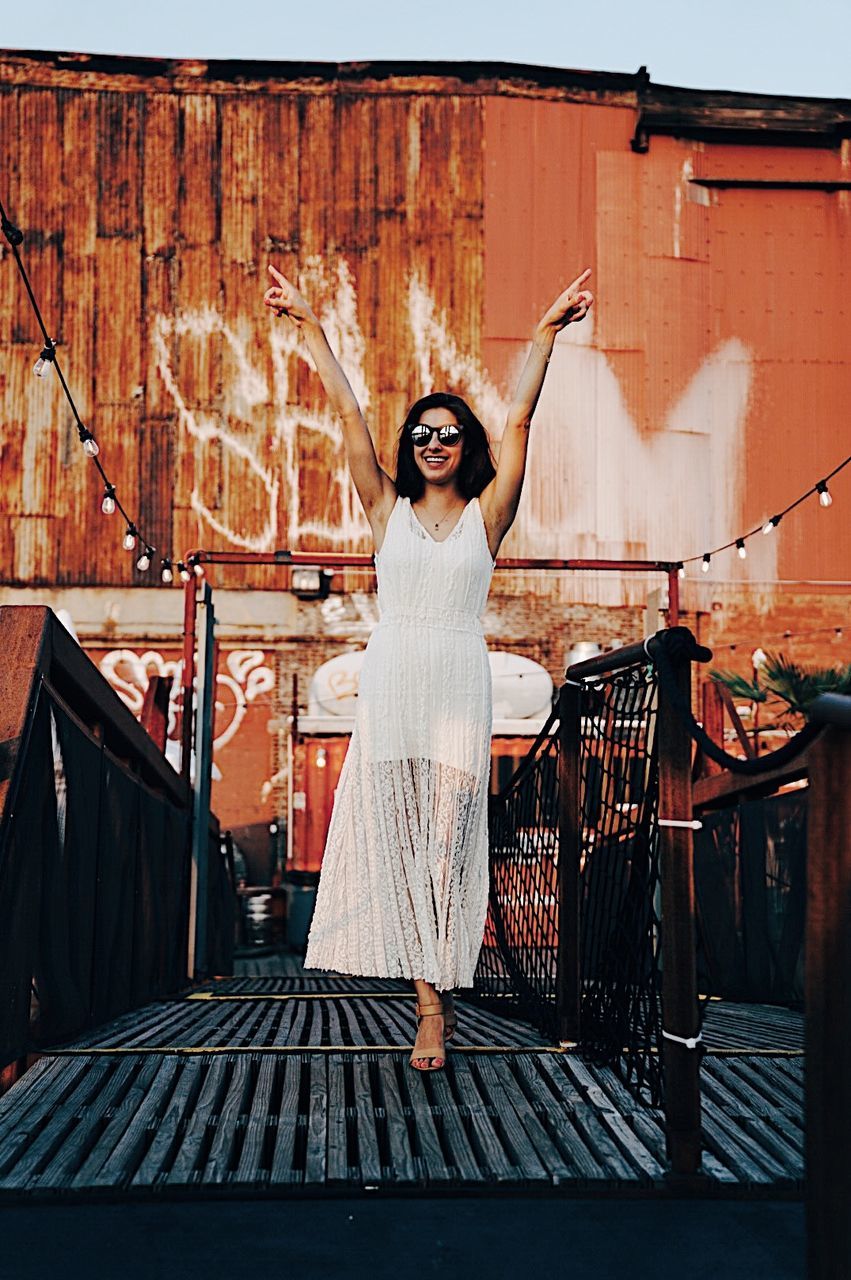 PORTRAIT OF HAPPY YOUNG WOMAN STANDING AGAINST BUILDING