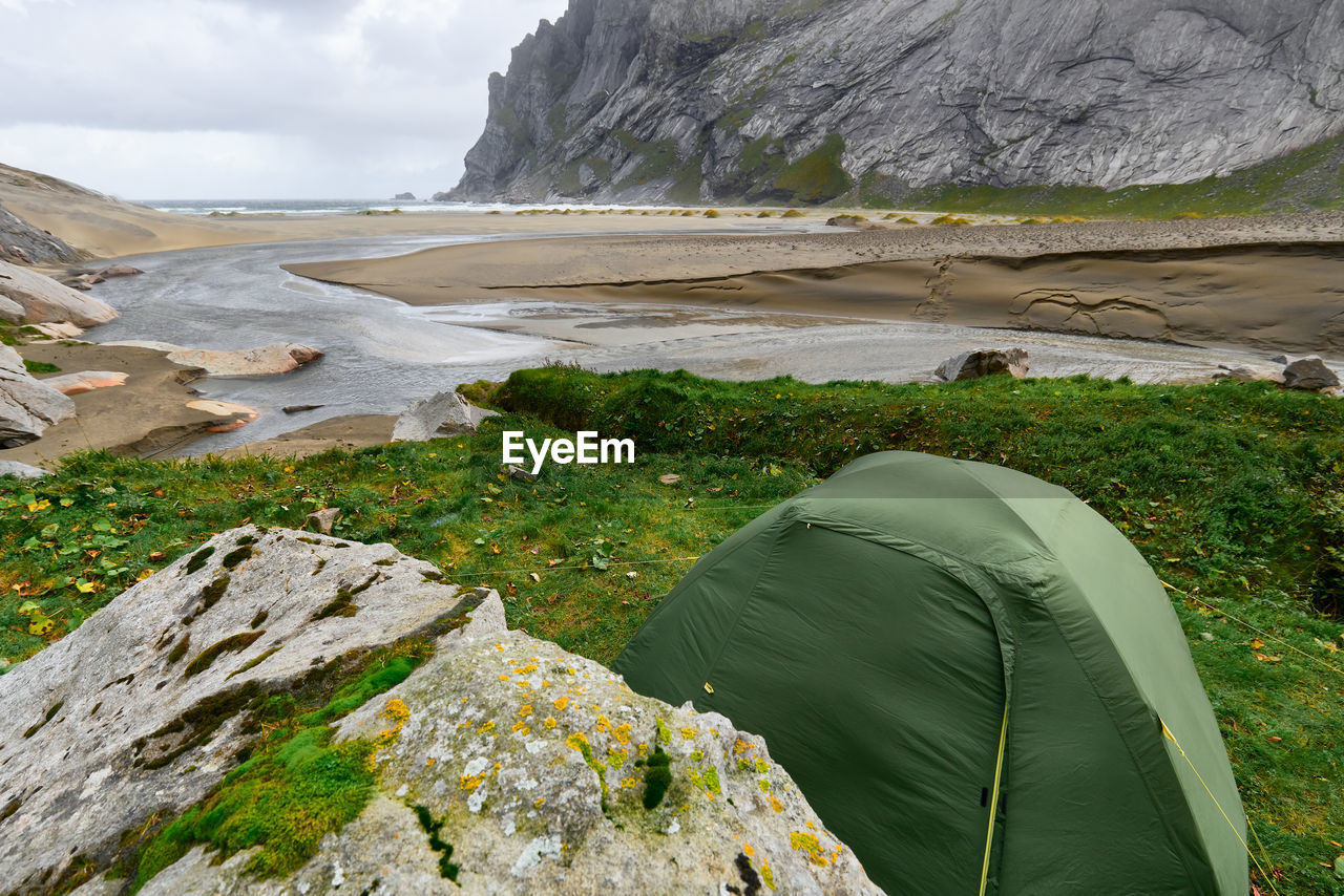 Green tent on a green grass hill at bunes beach with a view over the valley in lofoten norway.