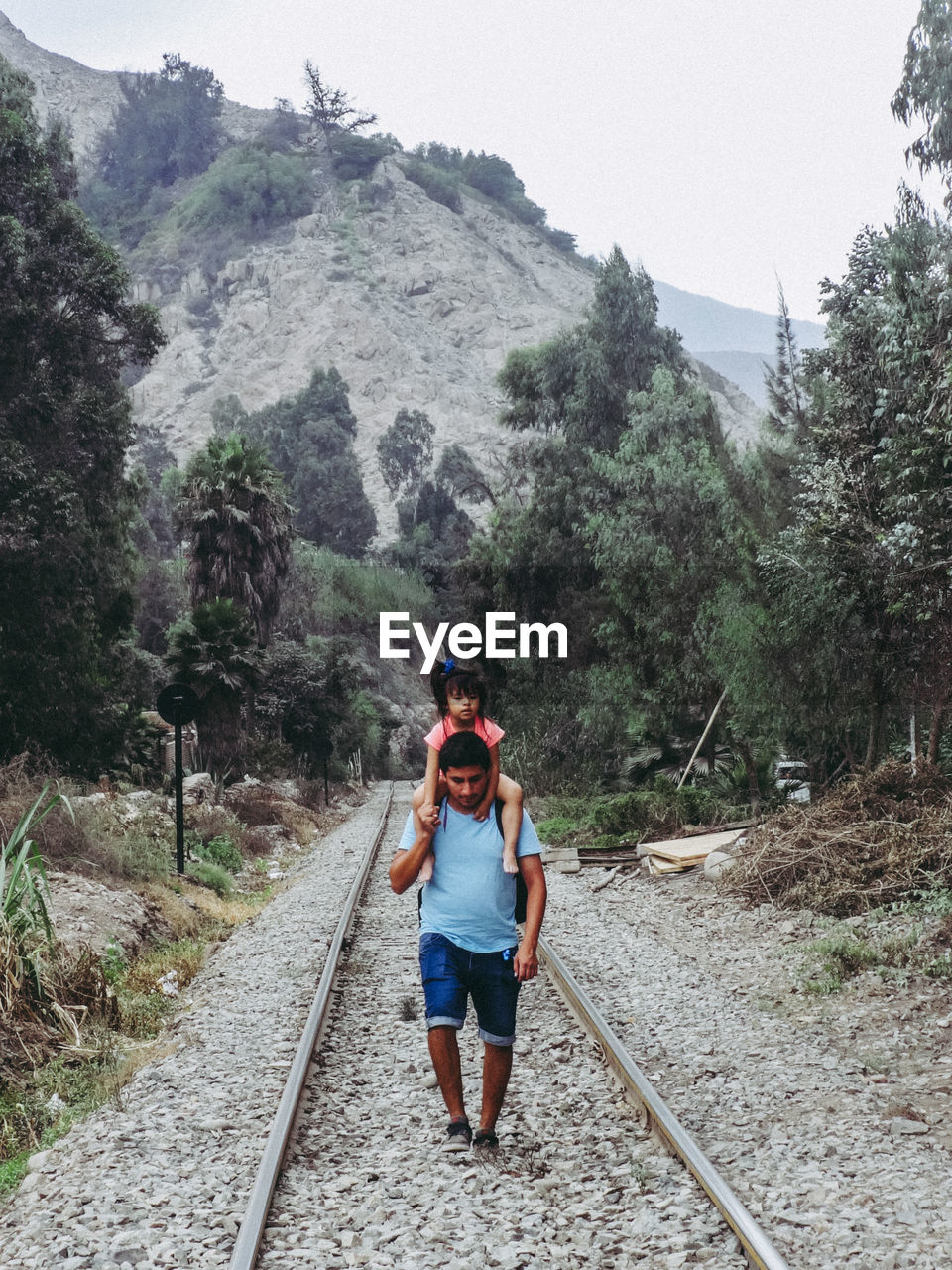 Man carrying daughter on shoulder while walking on railroad track