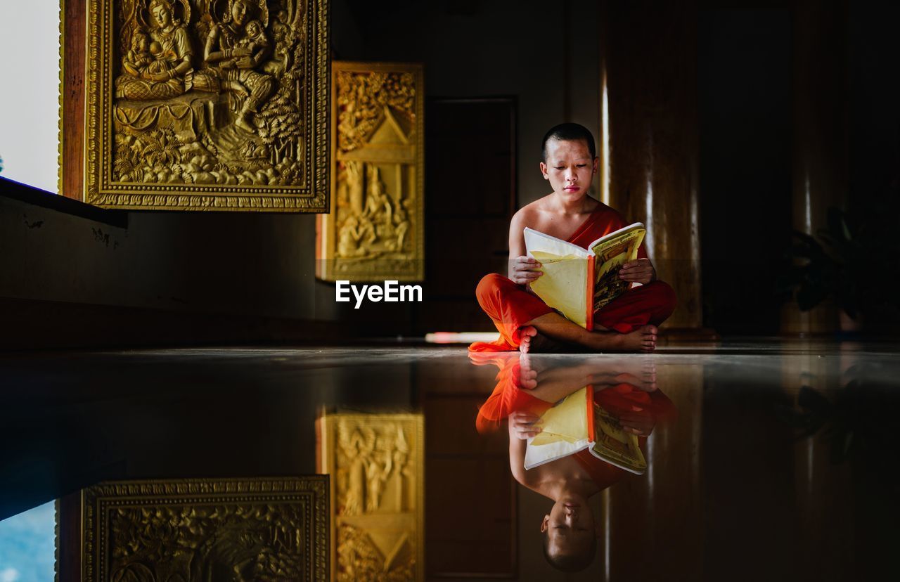 Monk reading book while sitting on floor in monastery