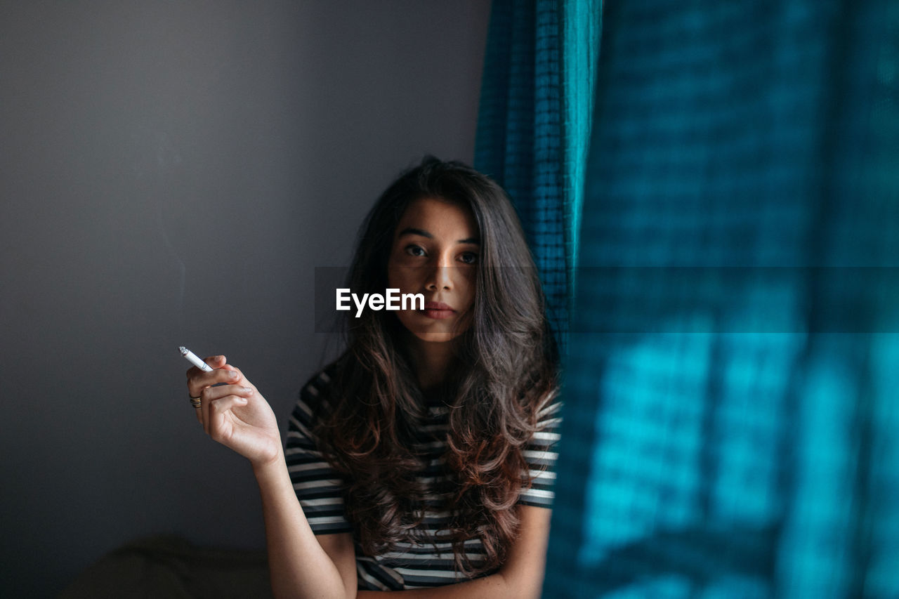 Portrait of woman smoking while sitting by window at home