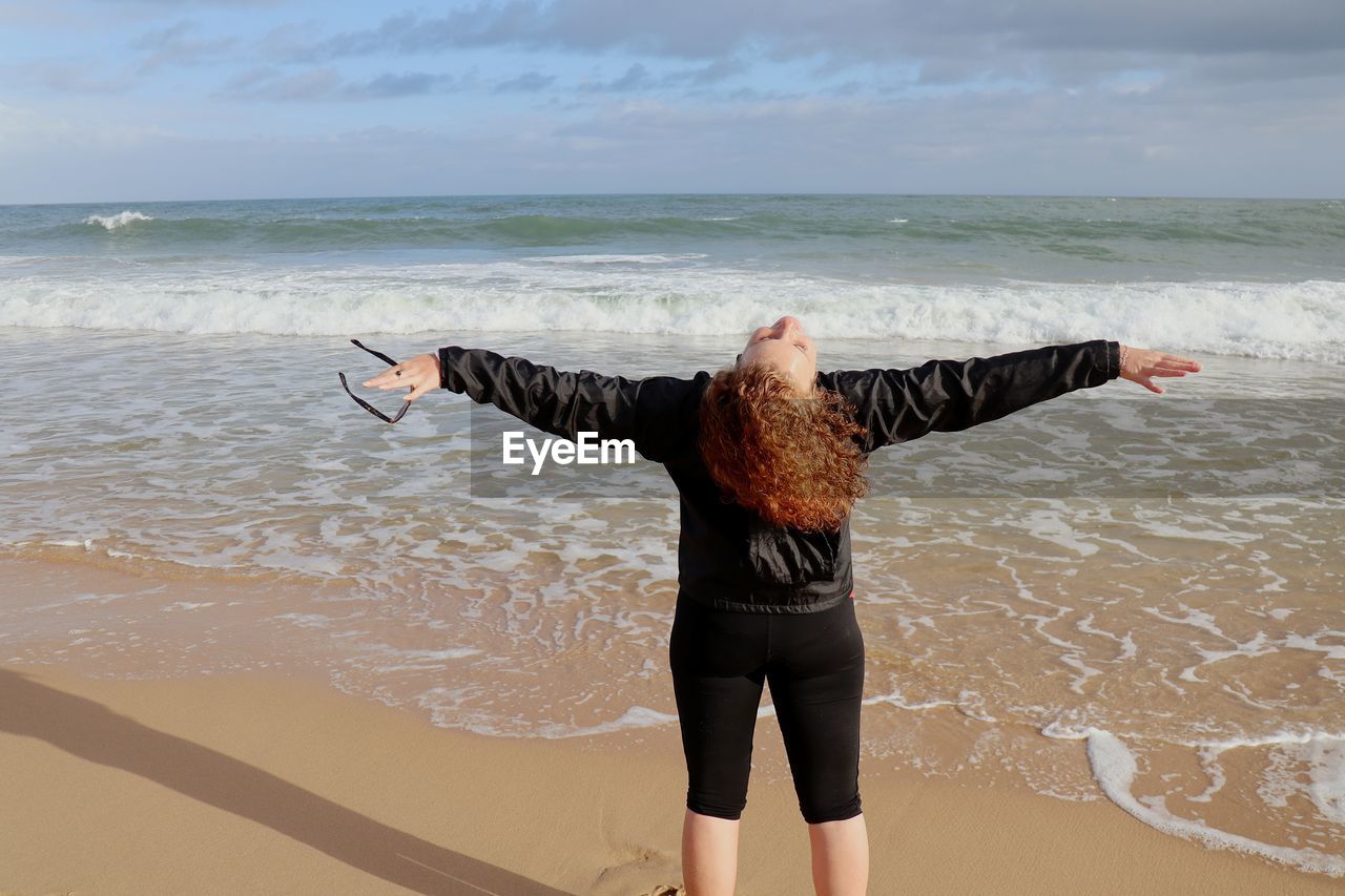 Rear view of woman with arms outstretched standing on beach