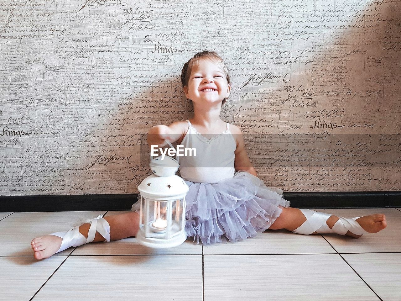 Portrait of cheerful girl holding lantern while doing splits on floor