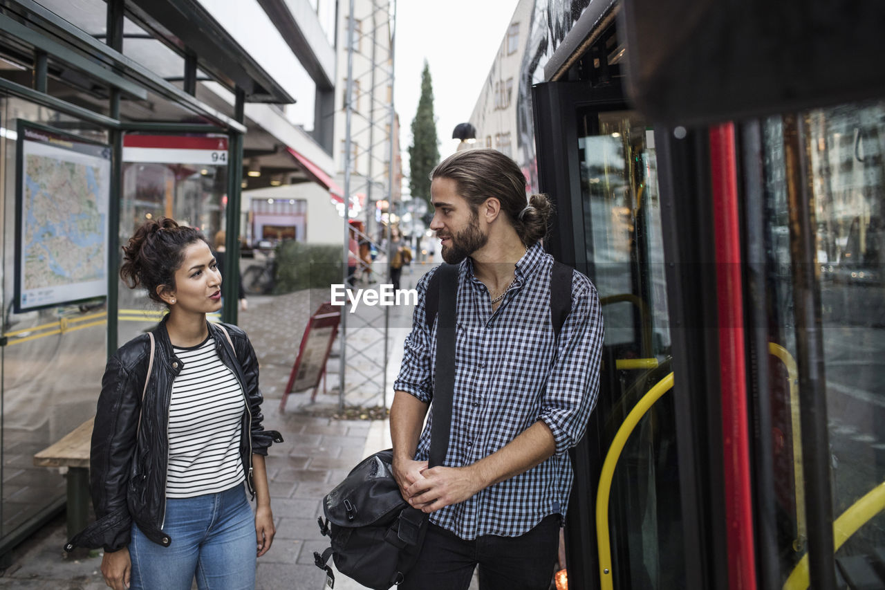 Friends talking while standing by bus in city