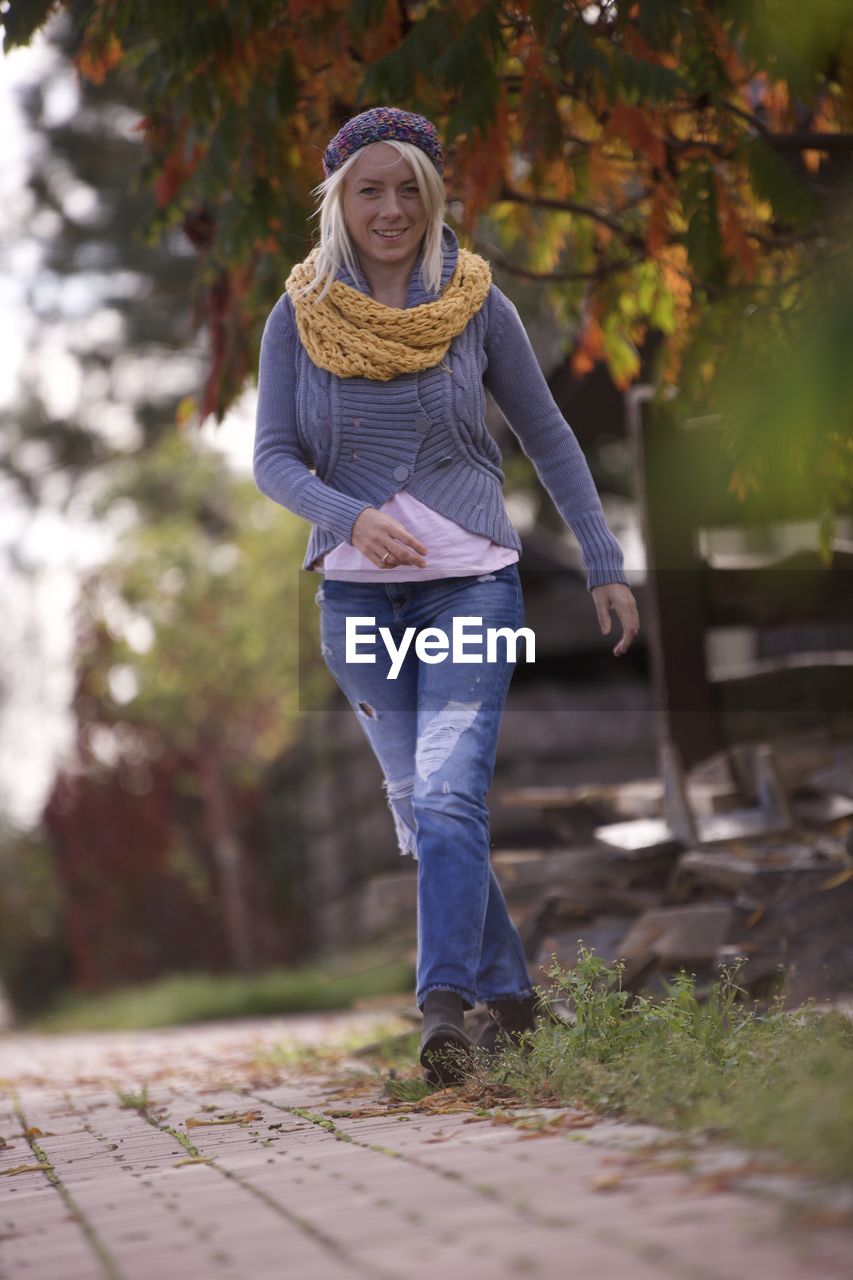 Blonde woman smiling dressed in wool sweater beret and wool scarf on goes autumn . colorful leaves