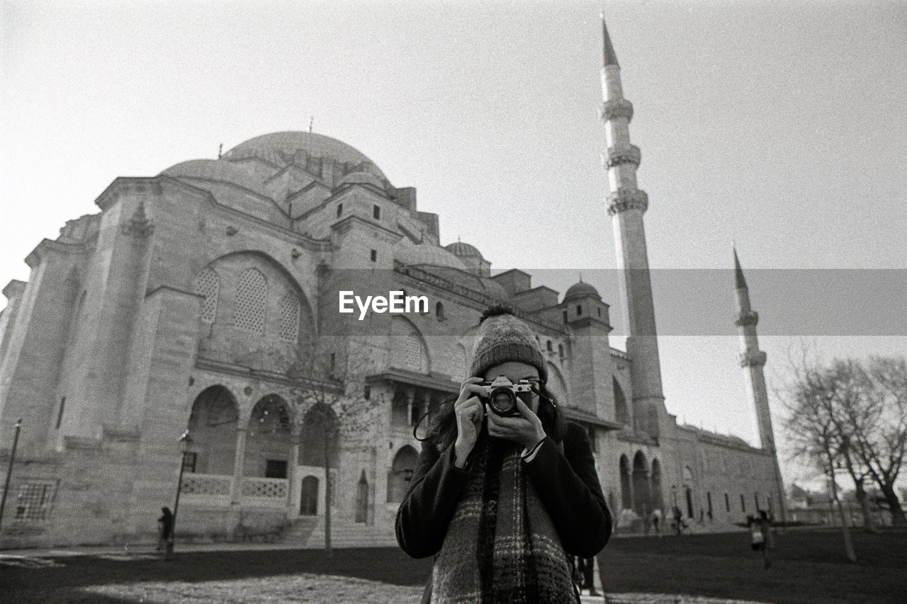 Woman photographing against building and sky