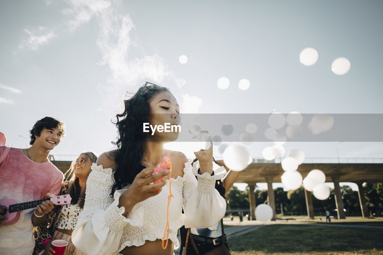 Young woman making smoke bubbles while enjoying with friends at music concert