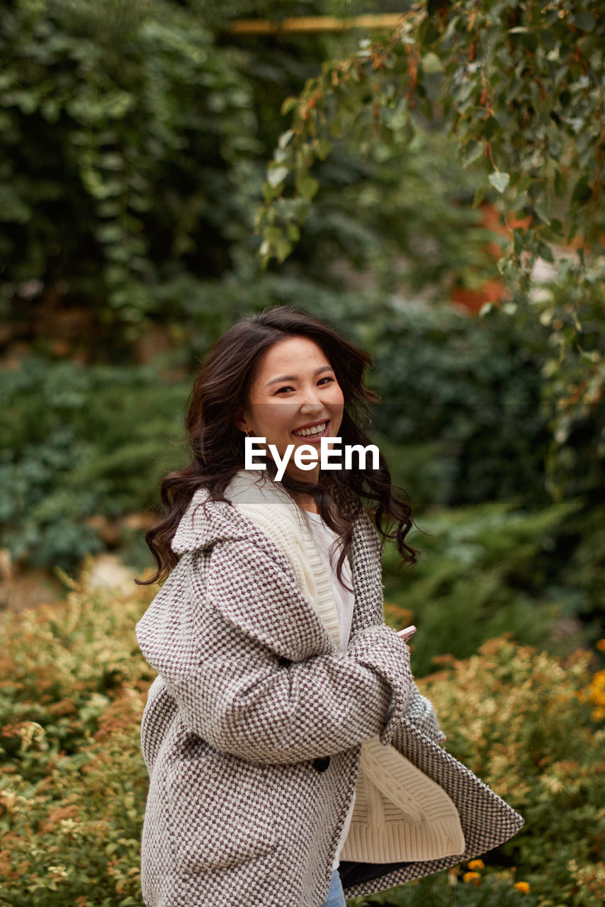 portrait of smiling young woman standing against plants