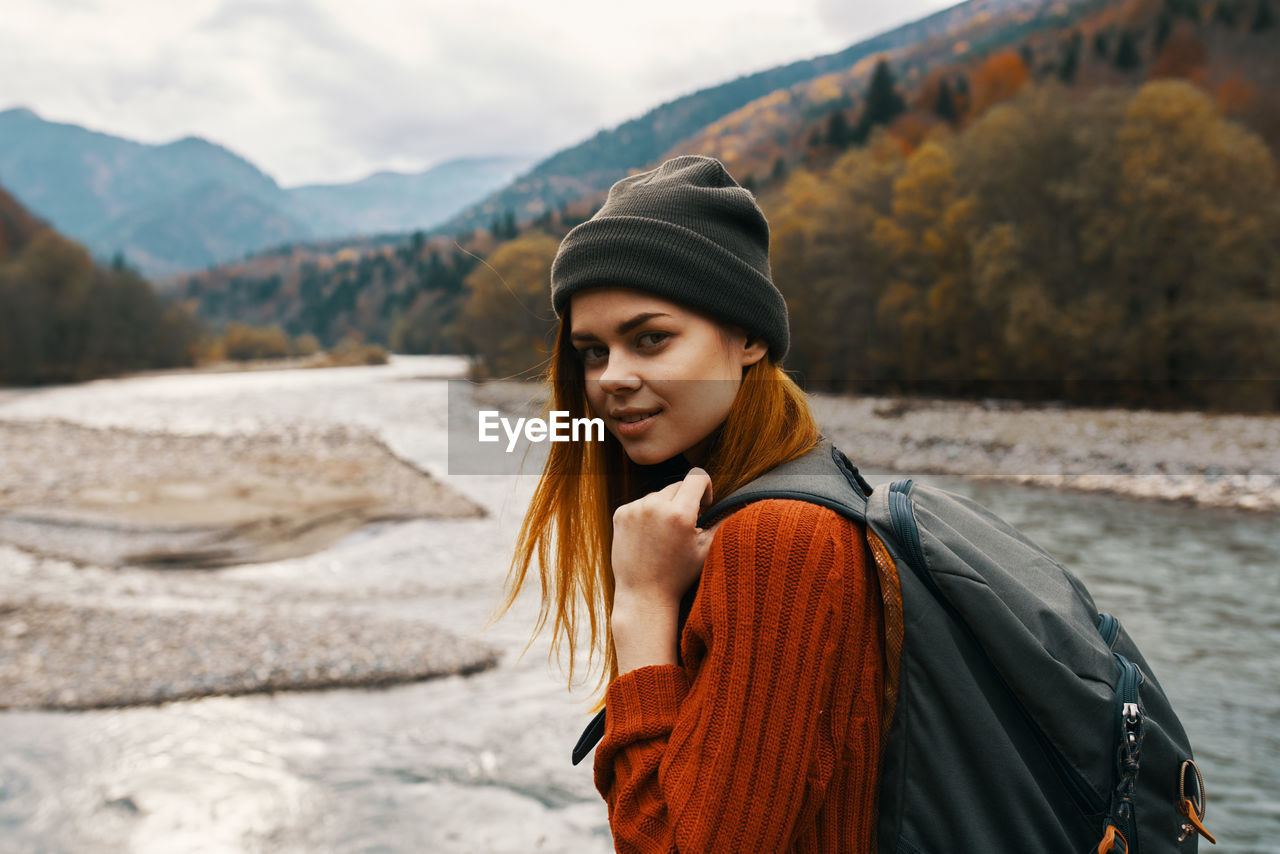 PORTRAIT OF BEAUTIFUL YOUNG WOMAN STANDING AGAINST MOUNTAINS