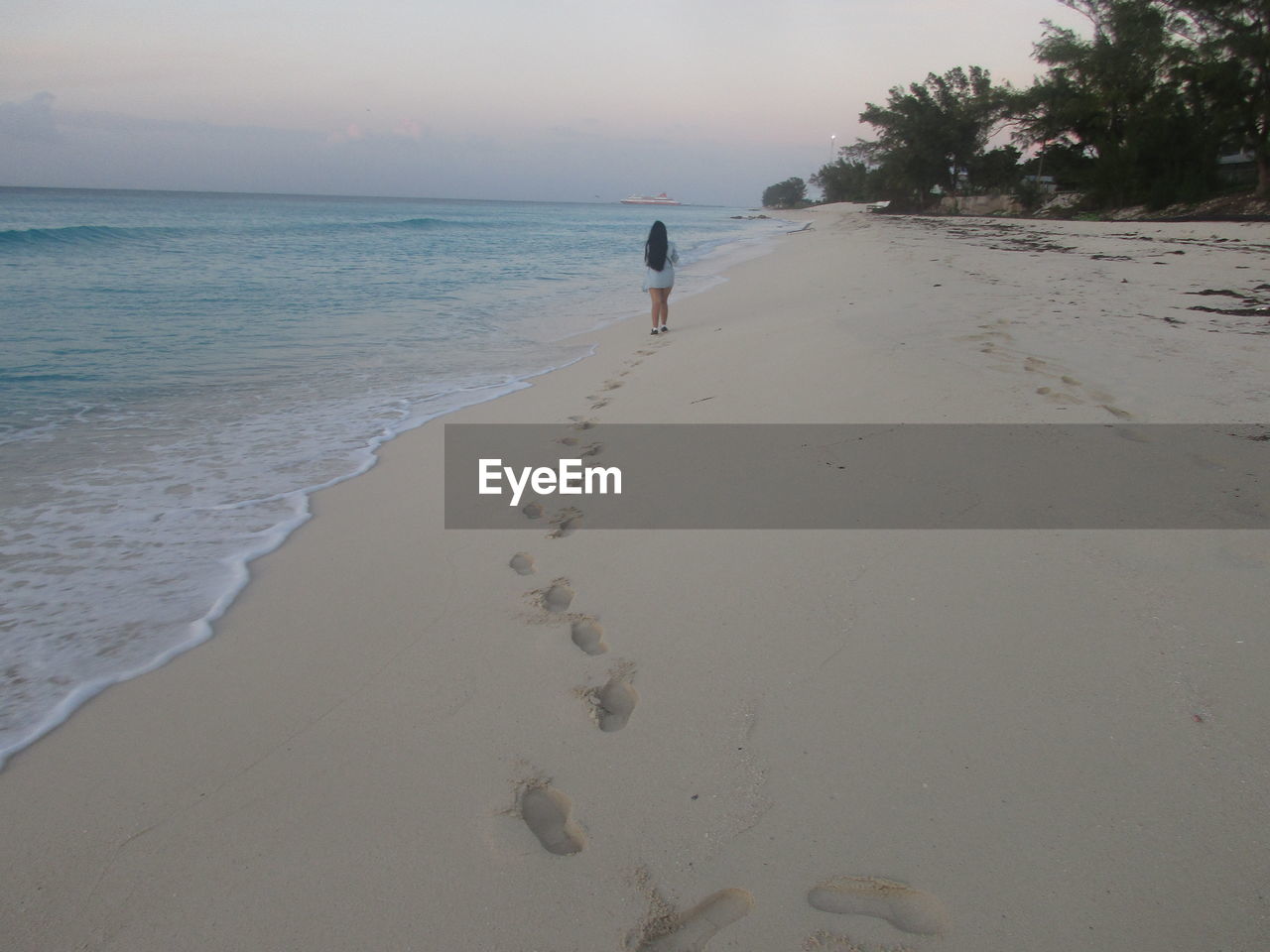 Rear view of woman walking at beach against sky during sunset