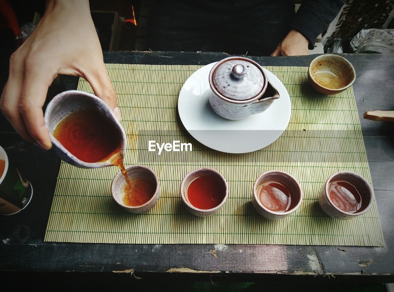 Cropped image of person pouring chinese tea in cup on table