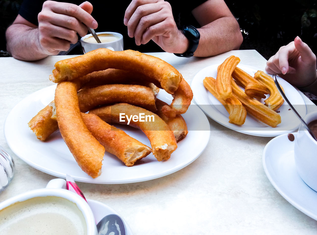 Midsection of man and girl having churros and coffee in a cafeteria from spain.