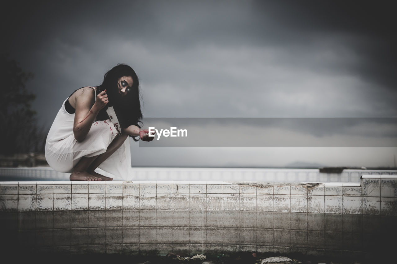 WOMAN SITTING ON RAILING AGAINST SKY