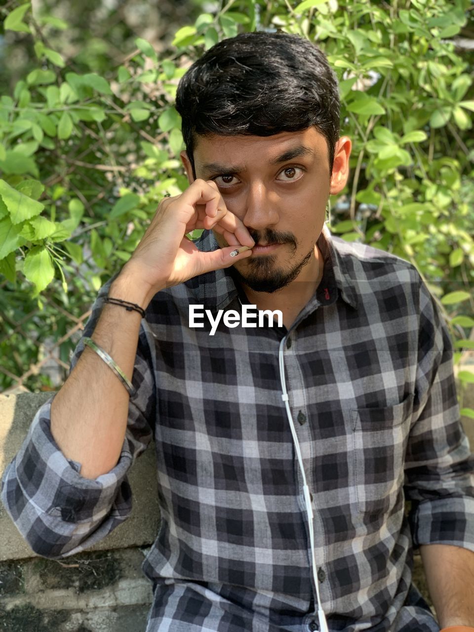 Portrait of young man smoking cigarette against plants