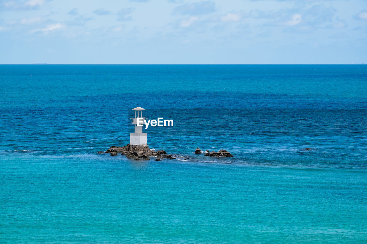 LIGHTHOUSE AMIDST SEA AGAINST BLUE SKY