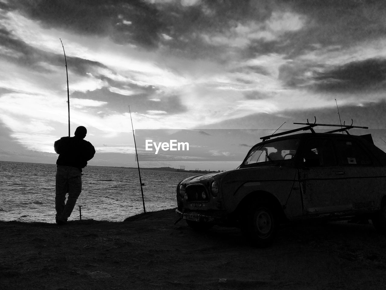 Man fishing in sea against sky during sunset