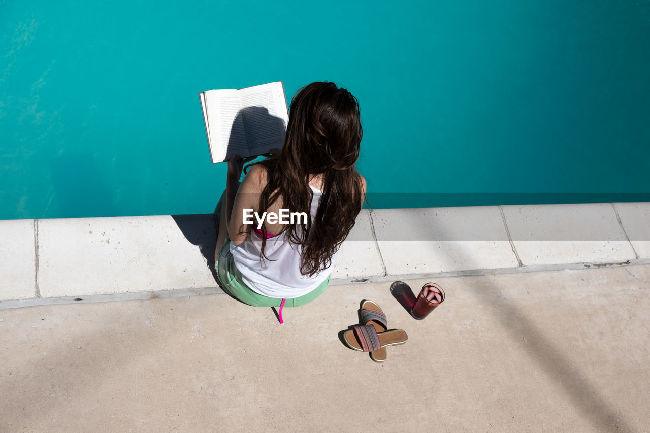 High angle view of woman reading book at poolside