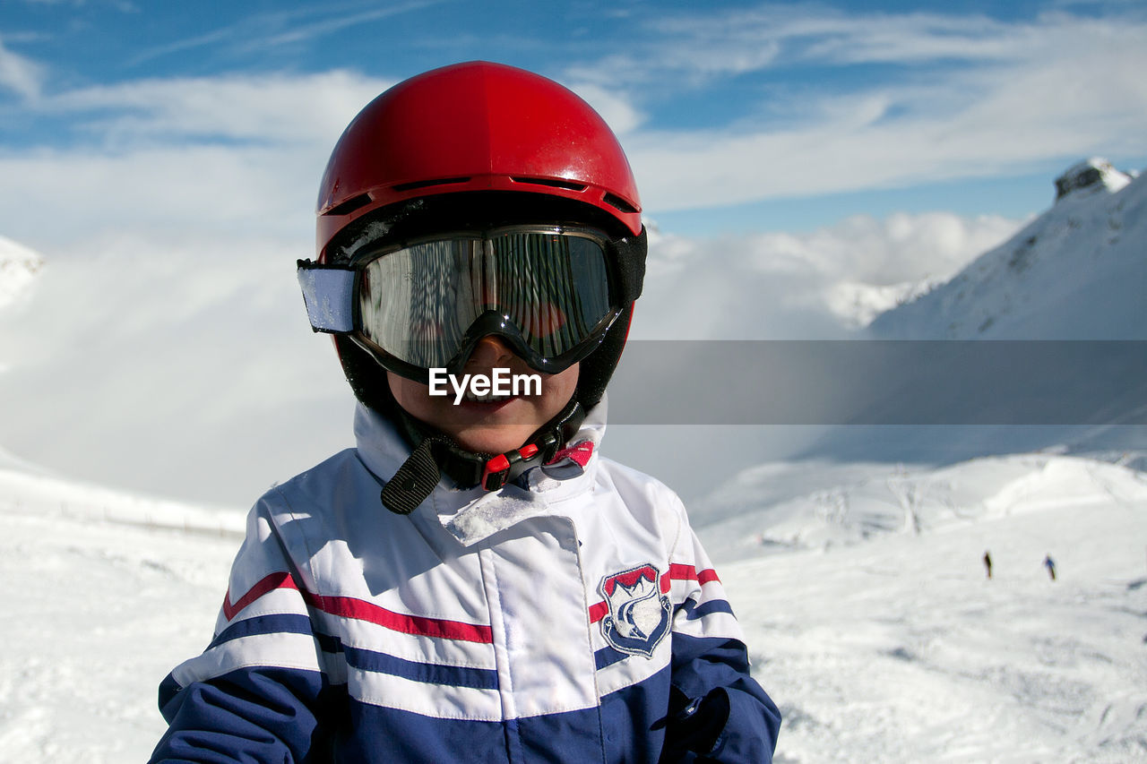 Portrait of cheerful smiling boy in red helmet, ski goggles and white jacket in winter ski resort. 