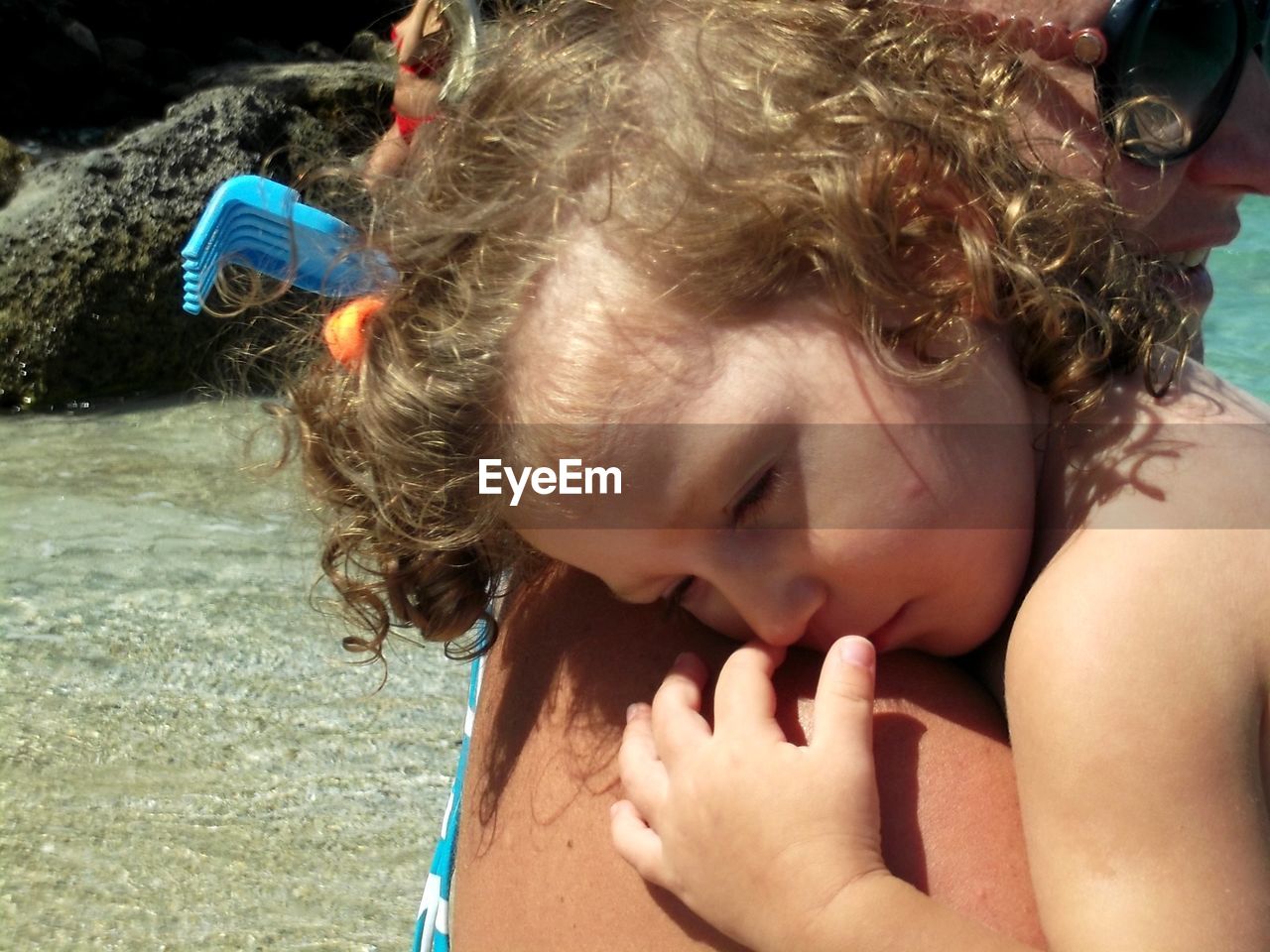 Close-up of mother carrying daughter by sea during sunny day