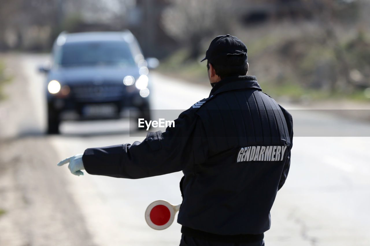 REAR VIEW OF MAN STANDING ON STREET AT CITY