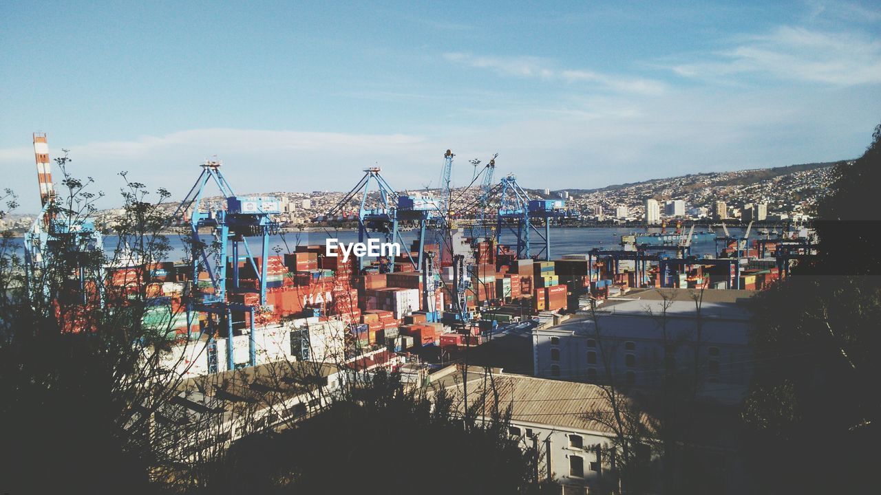 Cargo containers and cranes at harbor against sky
