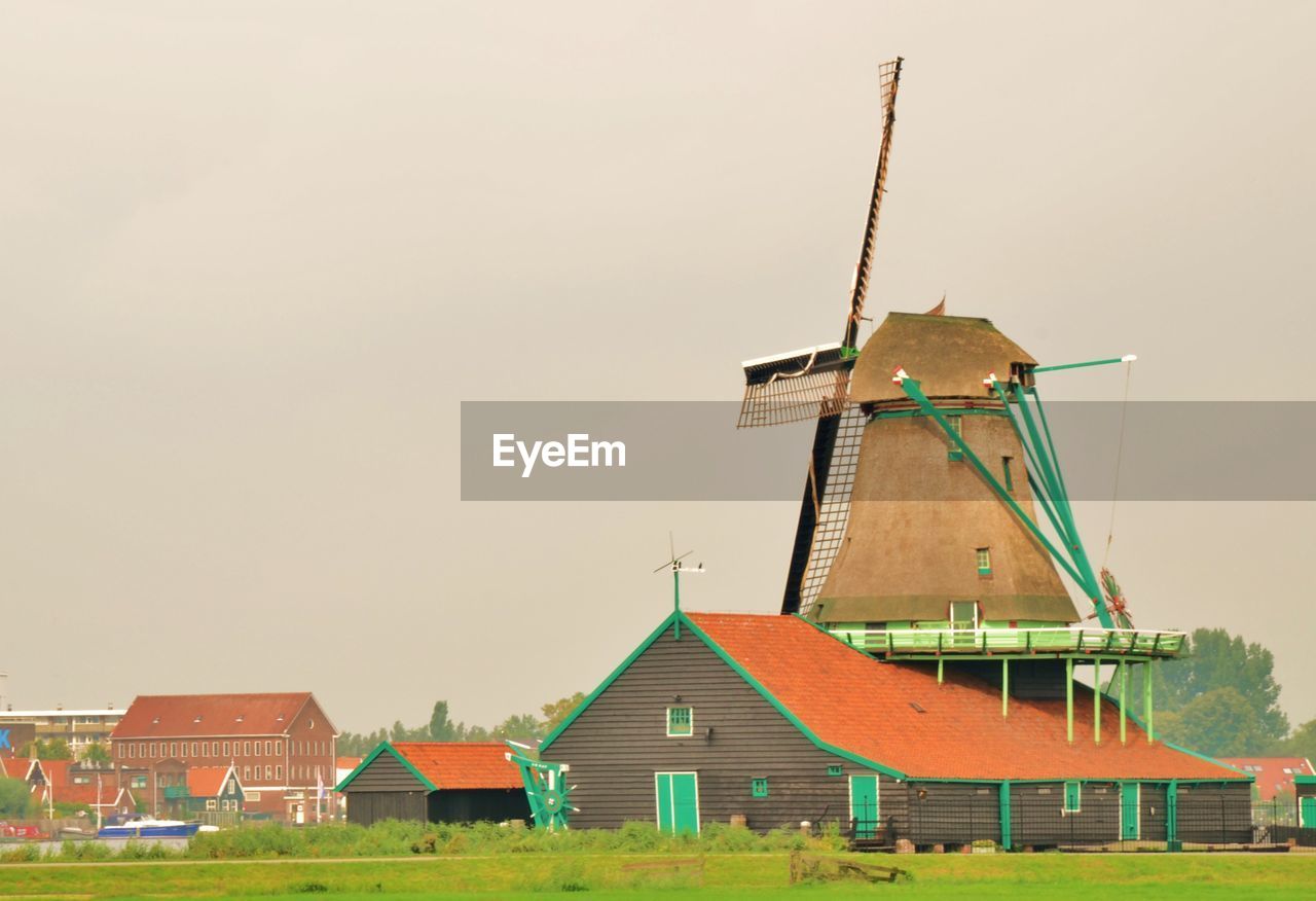 TRADITIONAL WINDMILL ON BUILDING BY WINDMILLS AGAINST SKY