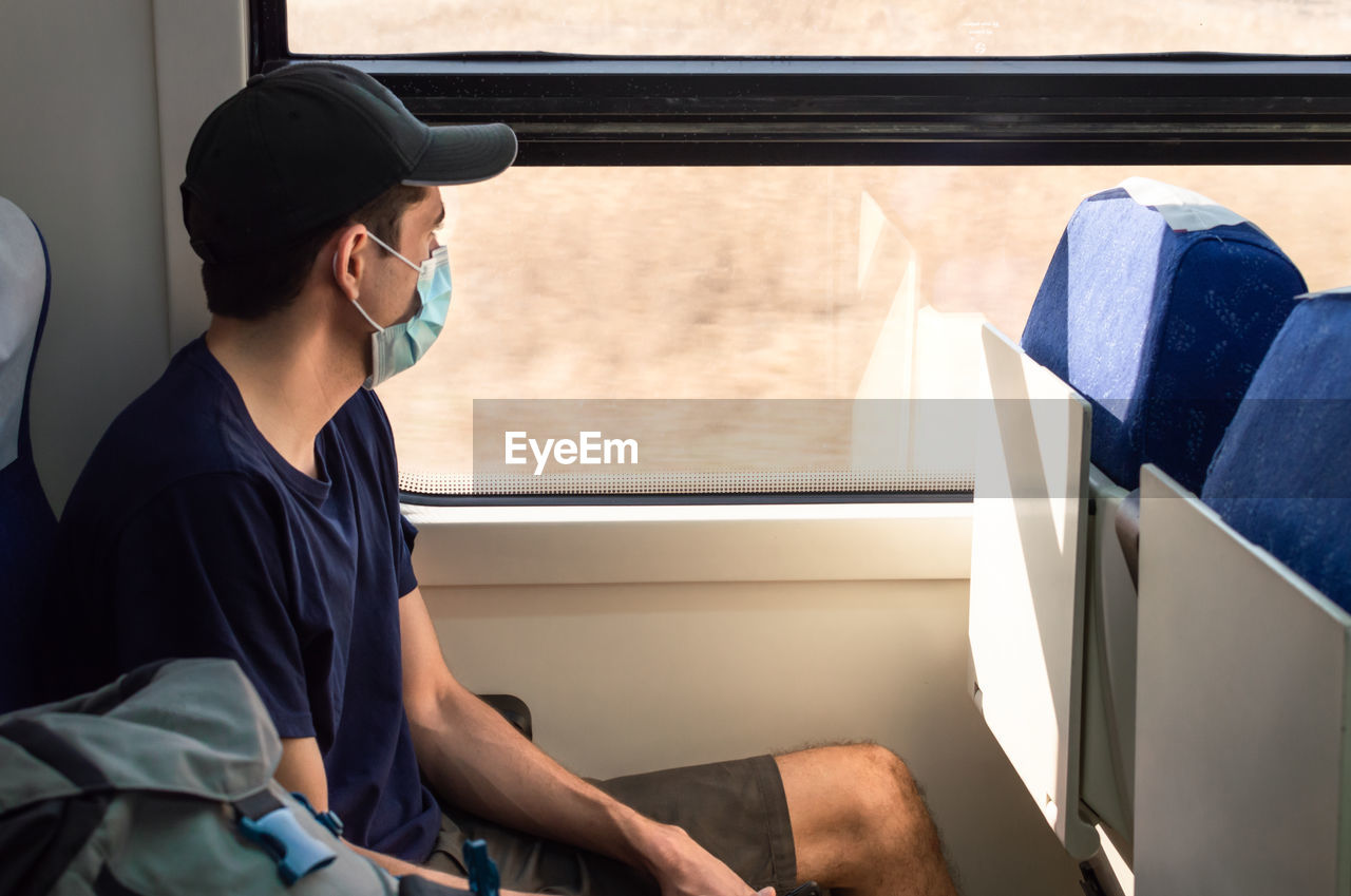 Young man with mask traveling by train during covid-19 pandemic.