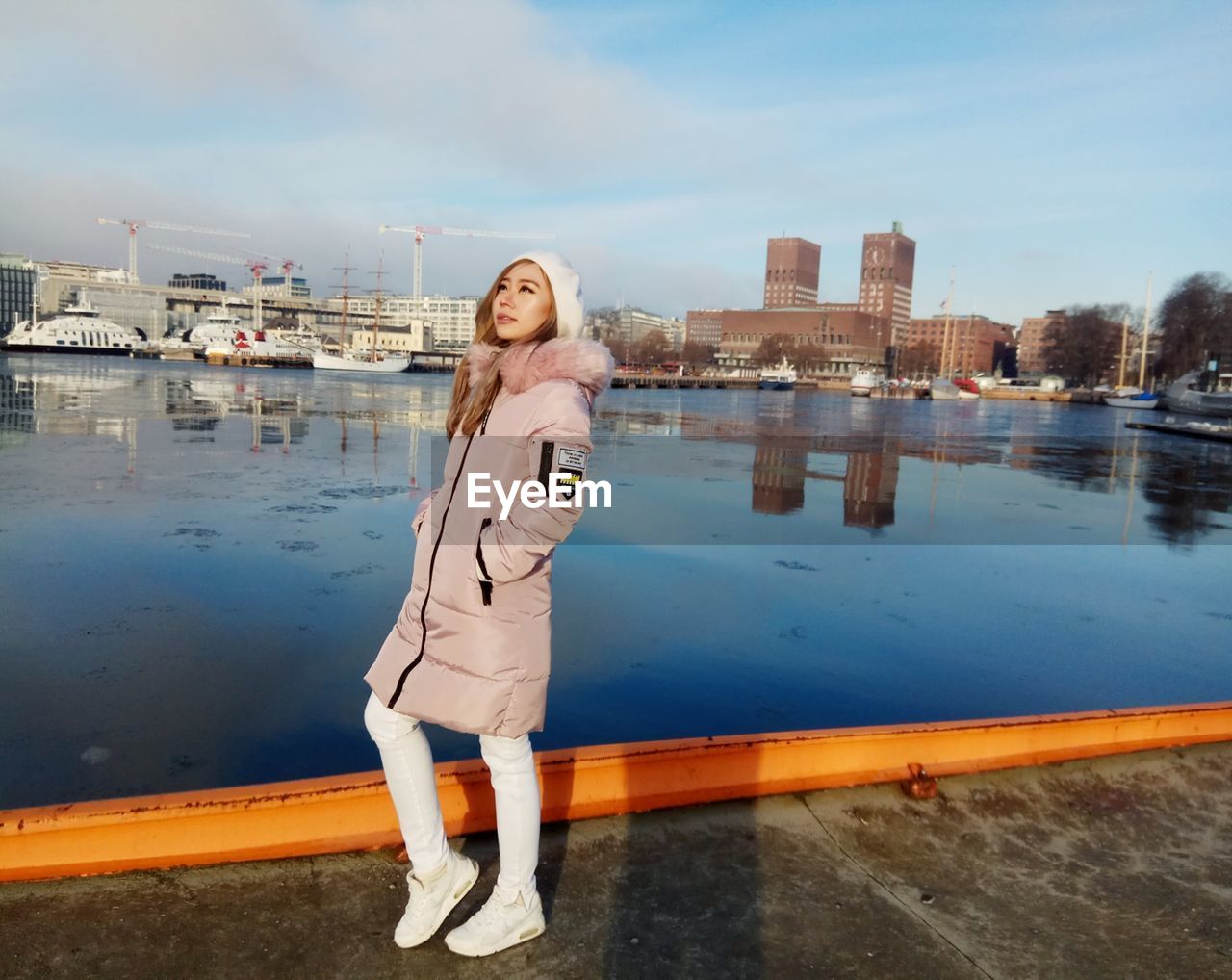 PORTRAIT OF YOUNG WOMAN STANDING BY RIVER IN CITY