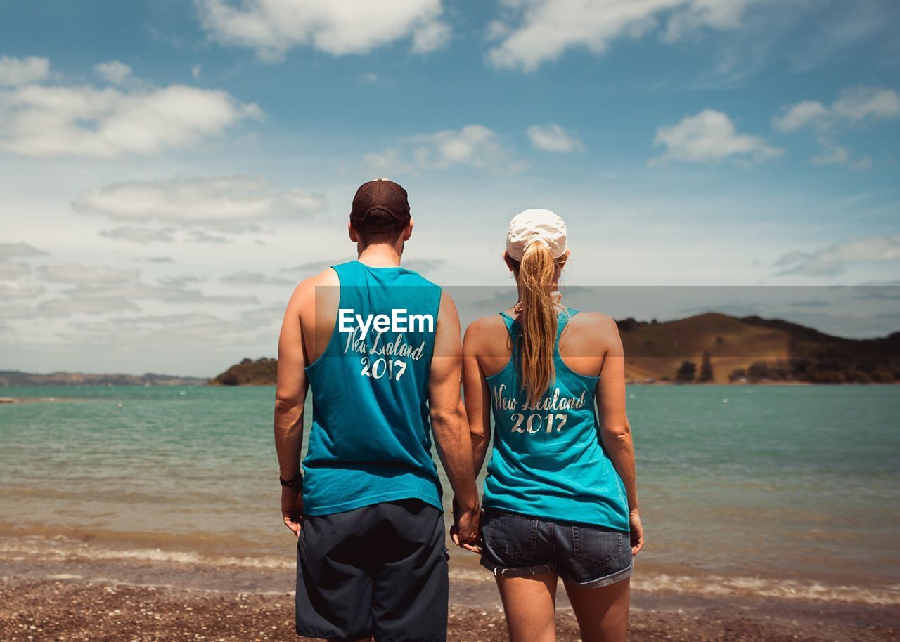 Rear view of couple standing at beach against sky