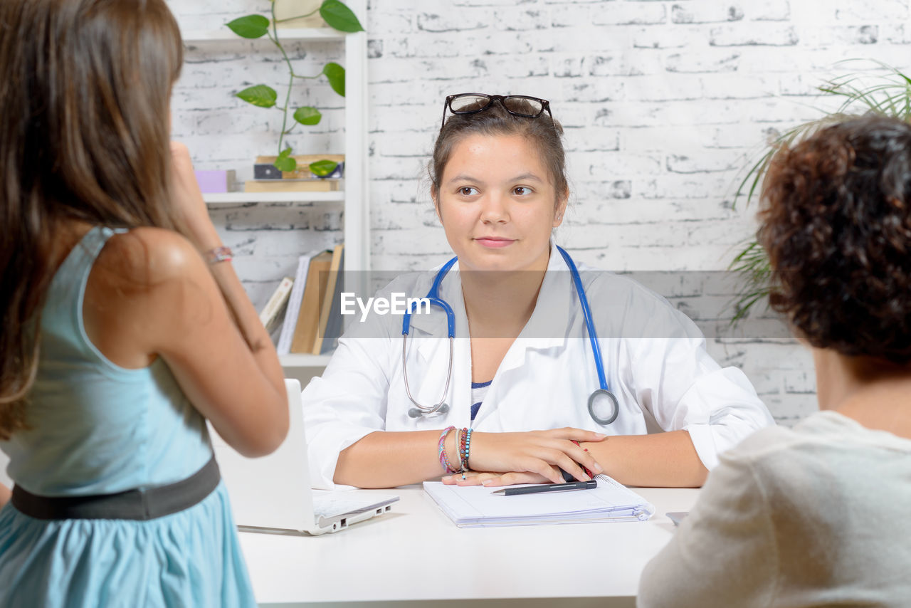 Rear view of woman with girl sitting with doctor