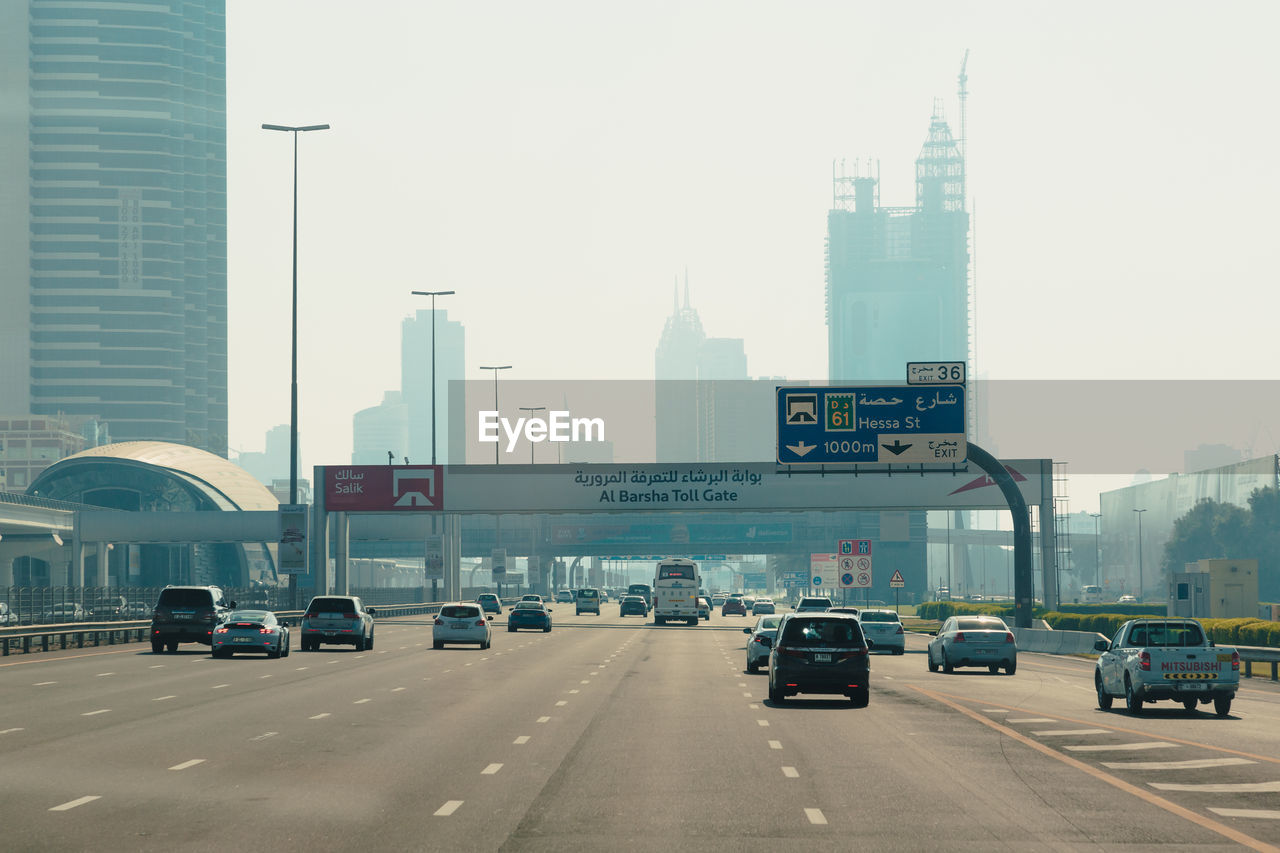 TRAFFIC ON ROAD BY BUILDINGS AGAINST SKY