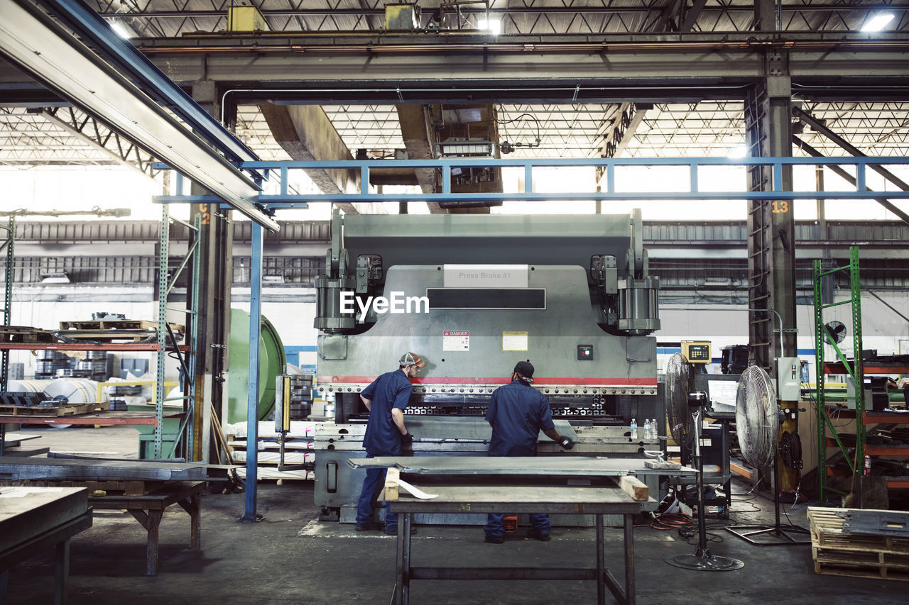 Rear view full length of workers working with machinery in industry