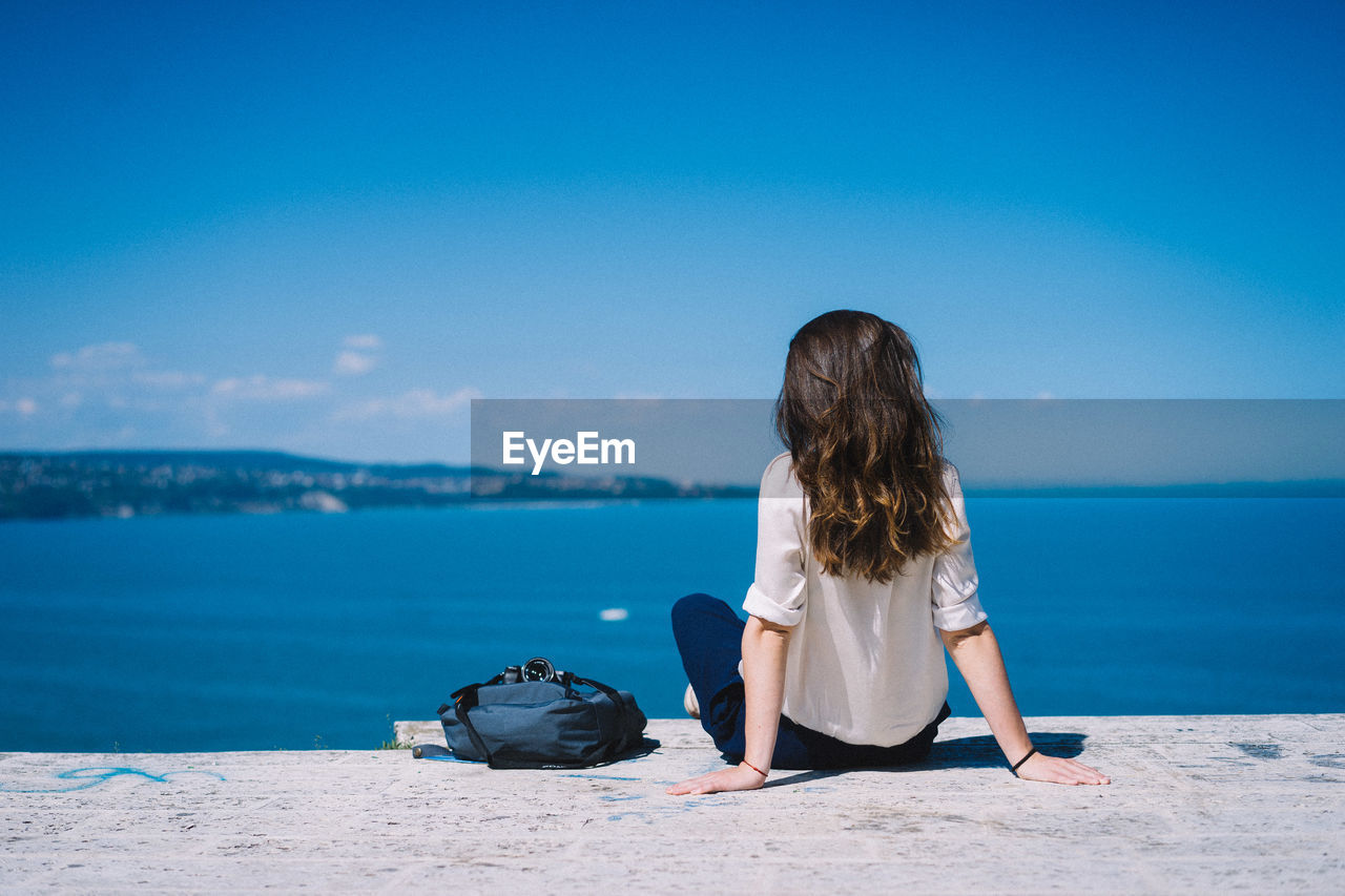 Rear view of woman sitting on shore against sea