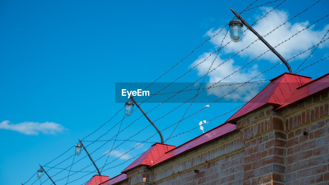 LOW ANGLE VIEW OF CABLES AGAINST BUILDING AGAINST SKY