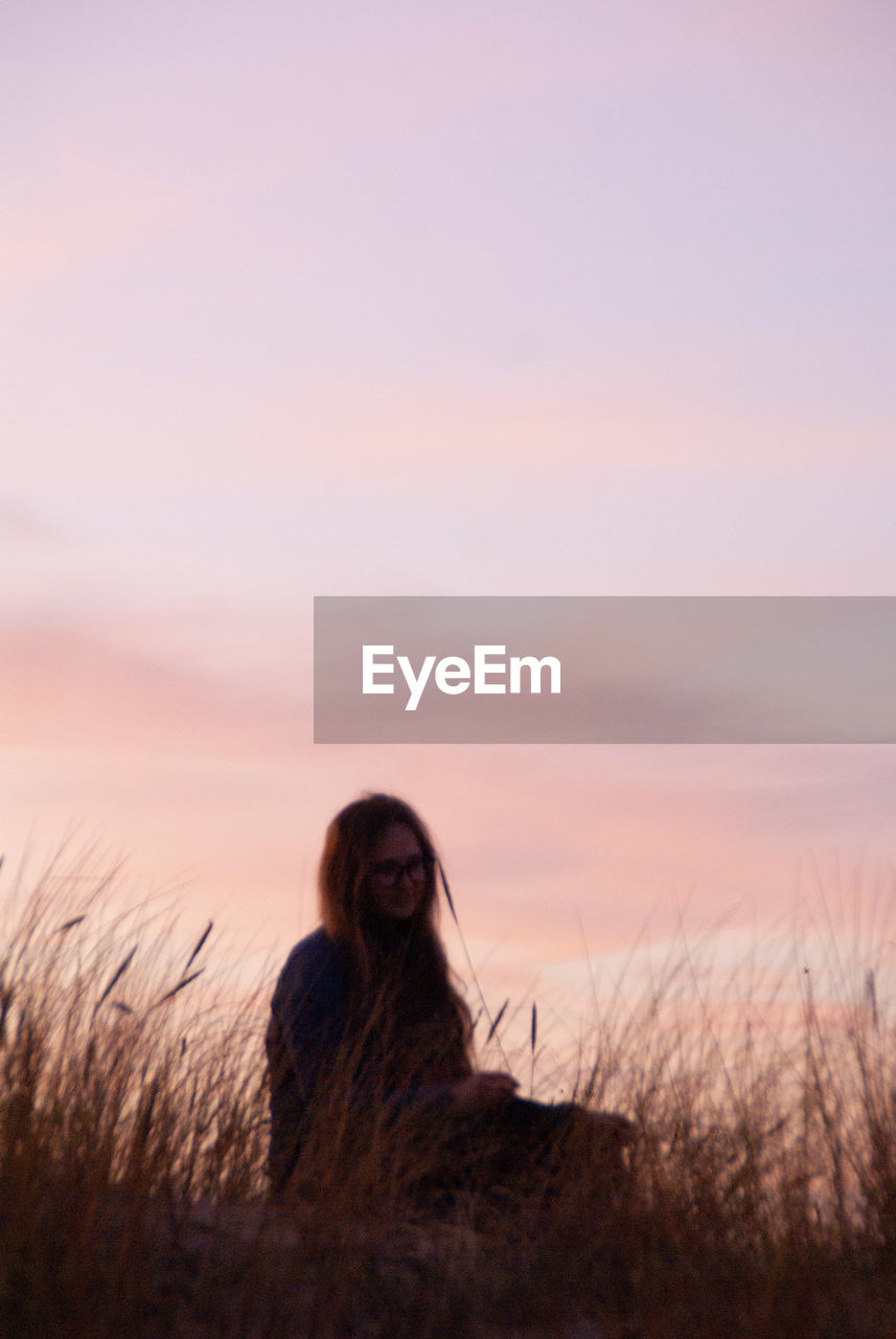 Low angle view of woman sitting on land against sky during sunset