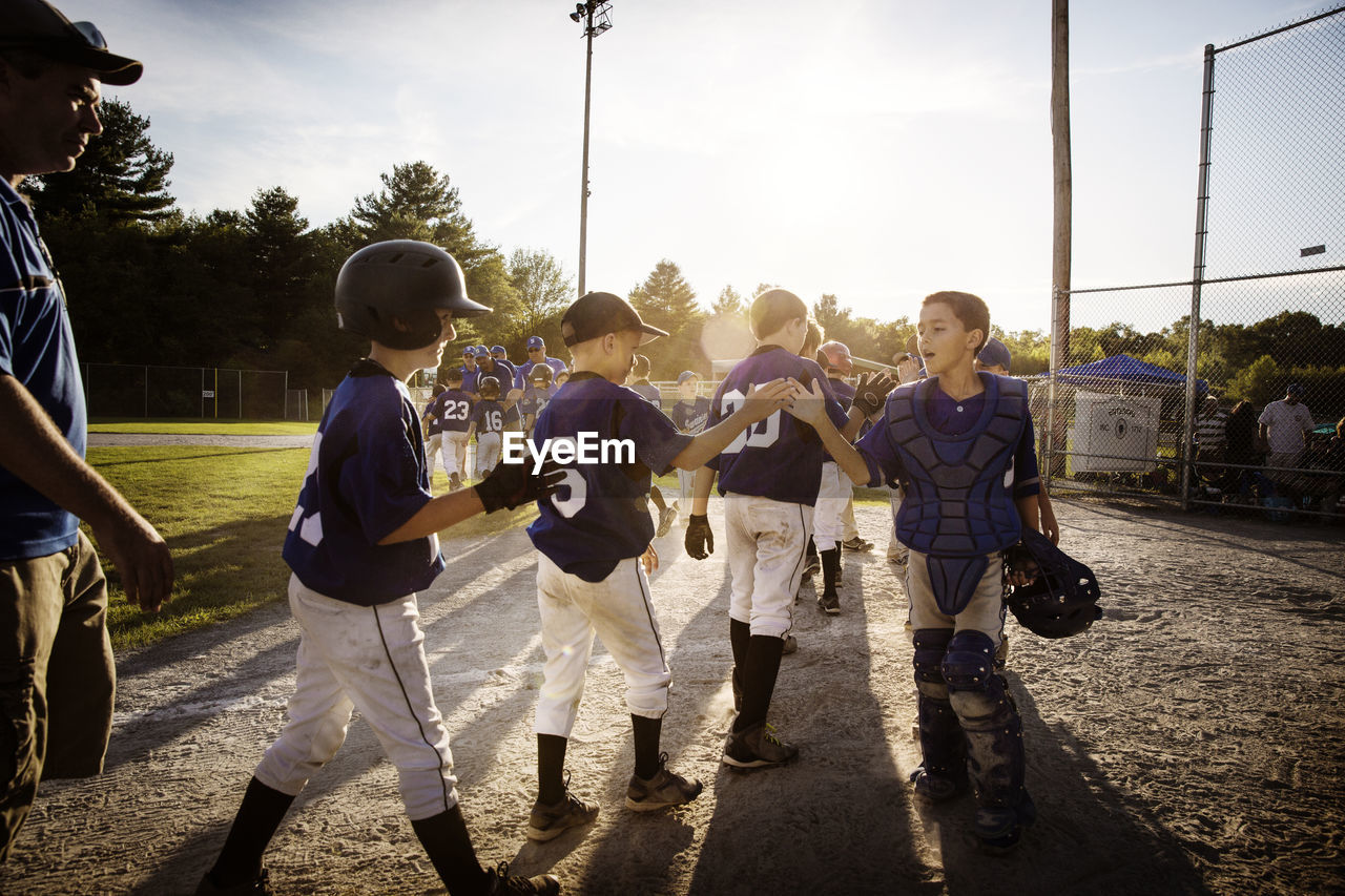 Baseball teams high fiving on field during sunset