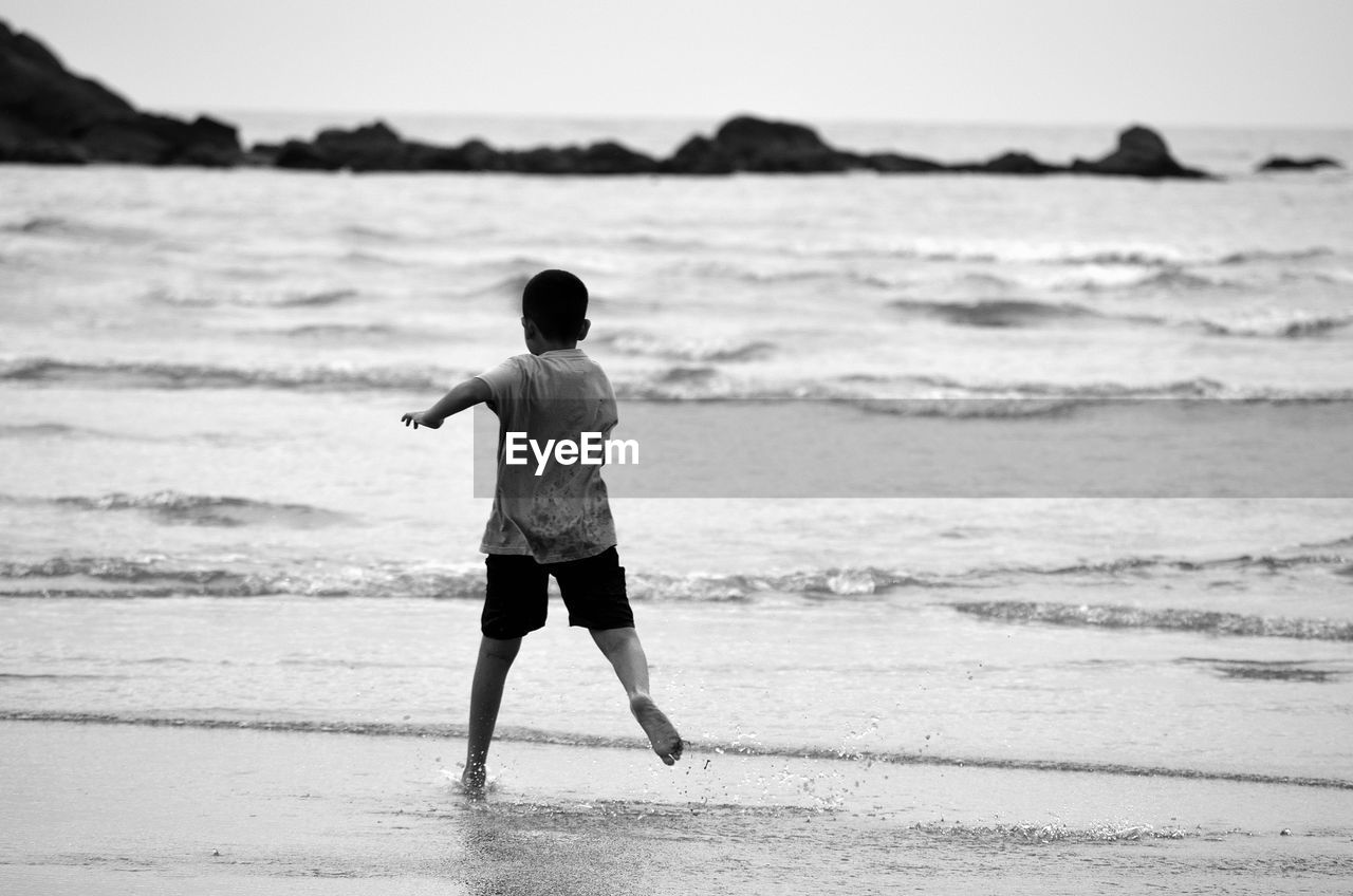 Rear view of boy running at beach against sky