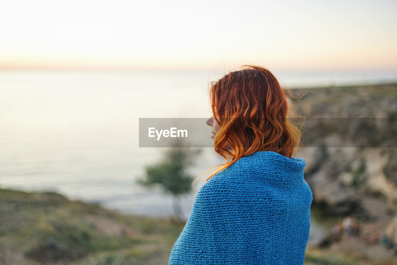 REAR VIEW OF WOMAN STANDING AT BEACH AGAINST SKY