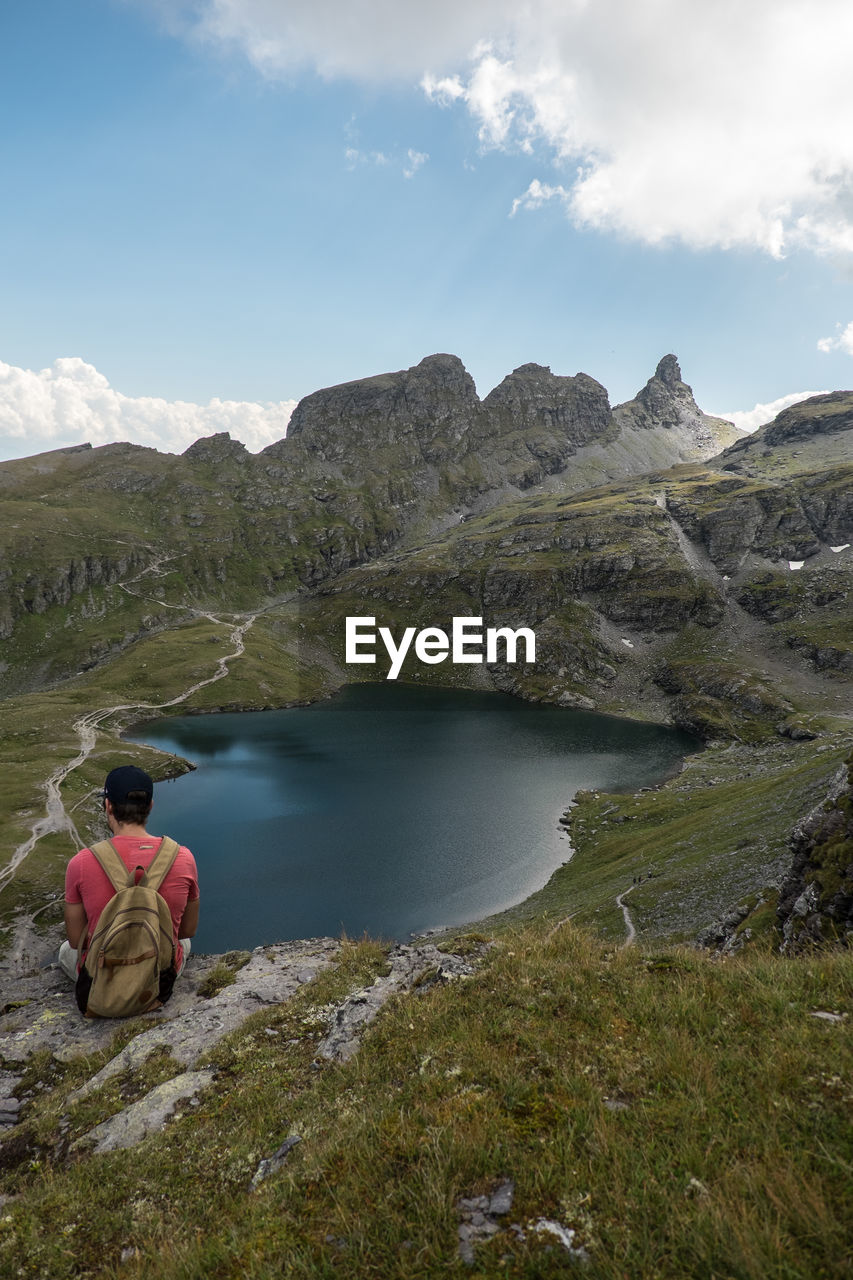 REAR VIEW OF MAN SITTING ON MOUNTAIN