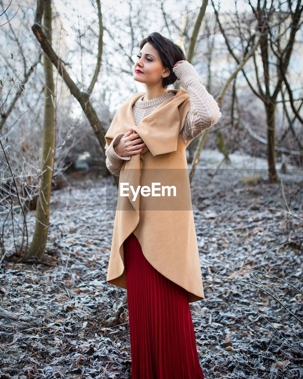 Woman in long dress standing against trees on field during winter