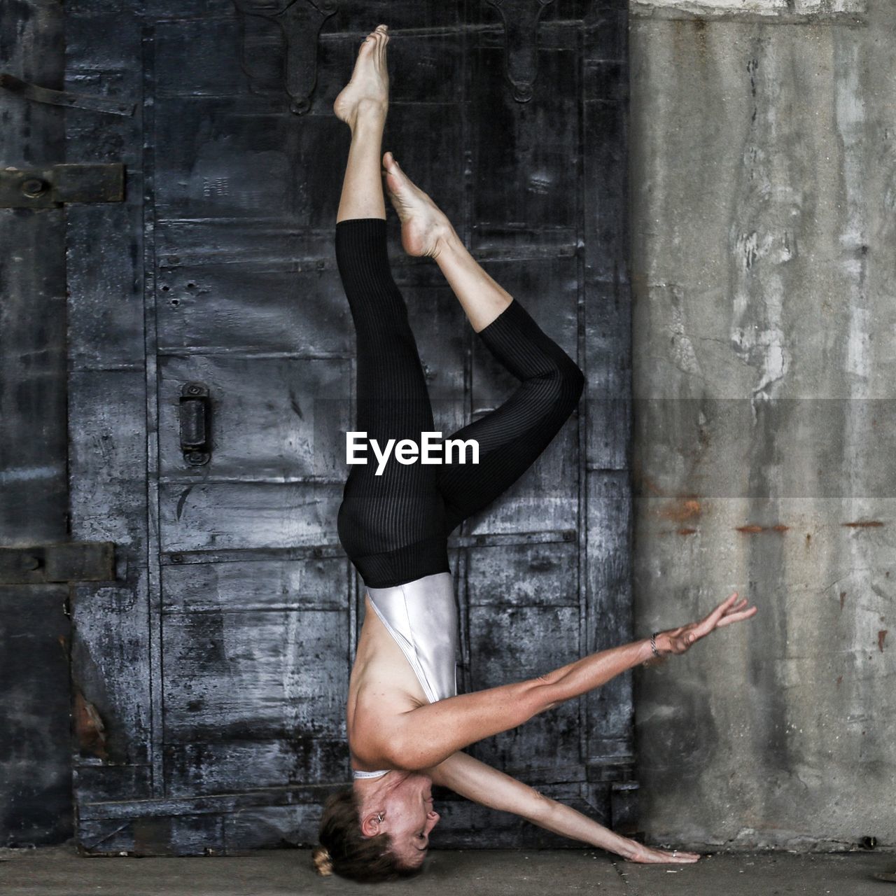 Full length of woman doing yoga headstand against wall