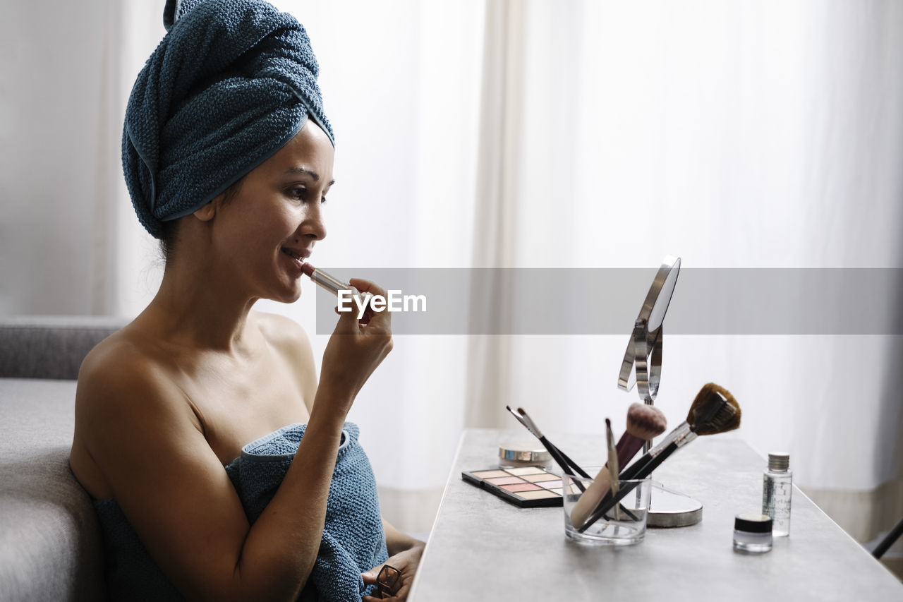 Side view of female applying natural colored lipstick during morning beauty routine