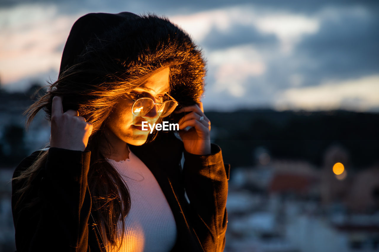 Young woman wearing hood standing outdoors during sunset