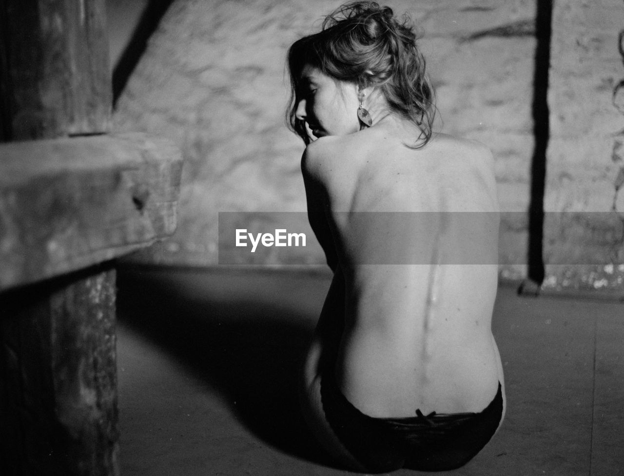 Rear view of sad naked woman sitting in darkroom