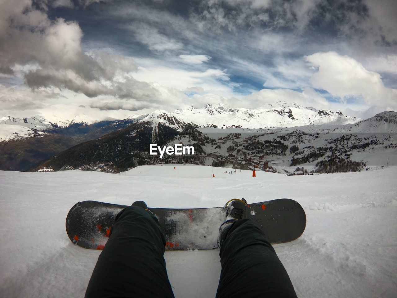 LOW SECTION OF PERSON ON SNOWCAPPED MOUNTAIN AGAINST SKY DURING WINTER